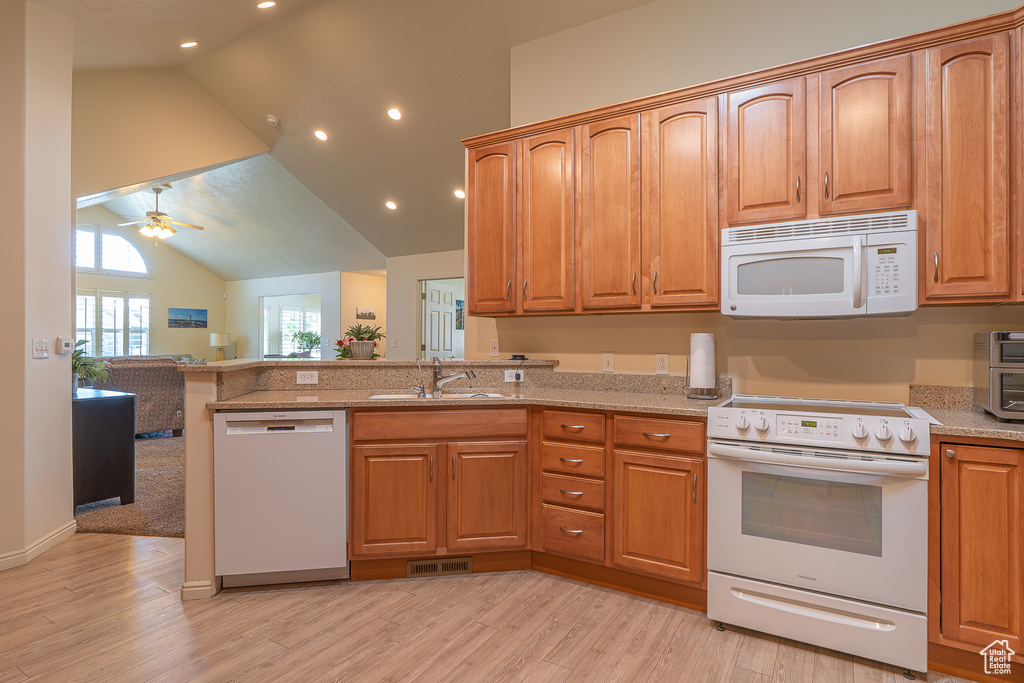 Kitchen with white appliances, light wood finished floors, a peninsula, open floor plan, and vaulted ceiling