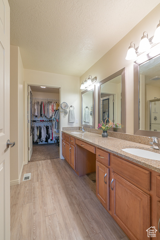 Bathroom with double vanity, wood finished floors, a textured ceiling, and a walk in closet