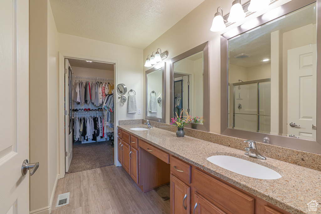 Bathroom featuring wood finished floors, double vanity, a spacious closet, a shower stall, and a textured ceiling