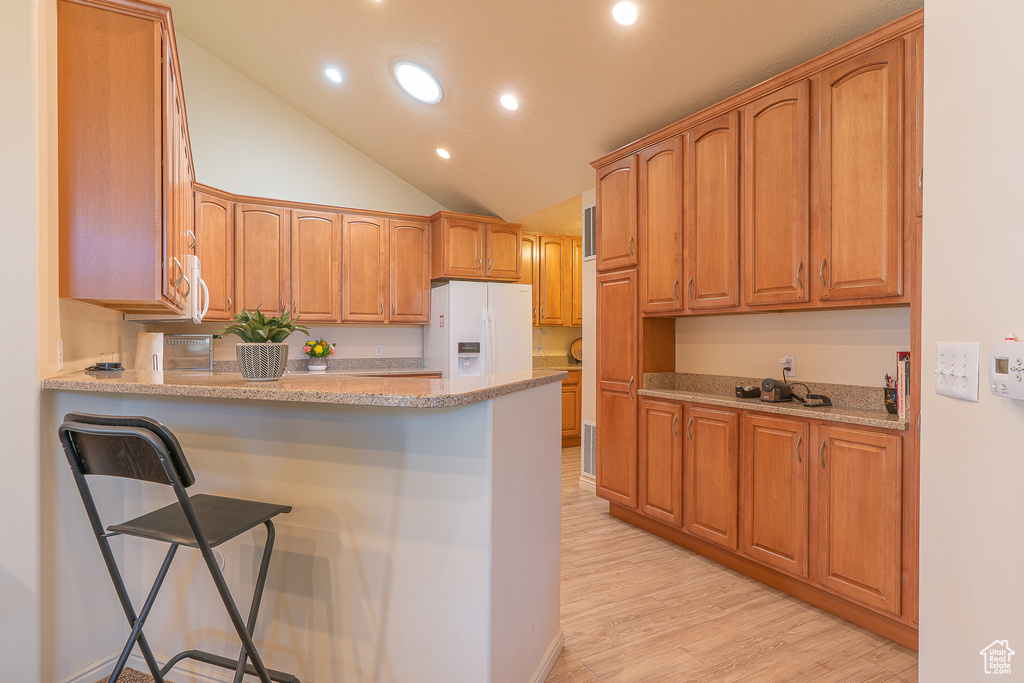 Kitchen featuring white fridge with ice dispenser, a peninsula, recessed lighting, light wood-style flooring, and a kitchen bar