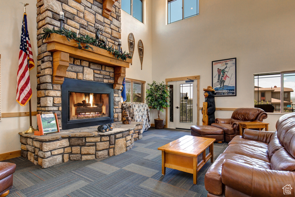 Living area with healthy amount of natural light, a high ceiling, a stone fireplace, and carpet flooring