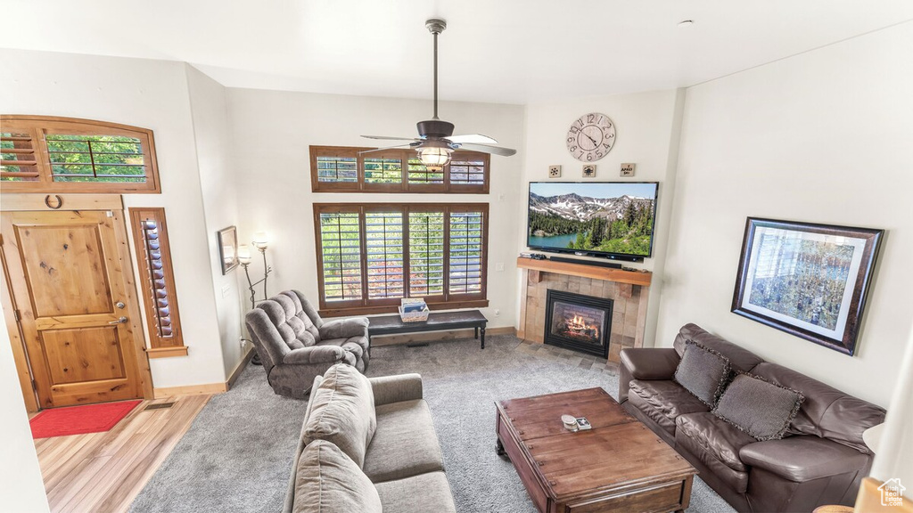 Living room with a tiled fireplace, ceiling fan, and wood finished floors