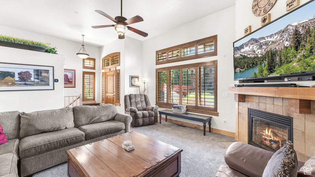 Living area featuring carpet flooring, a tiled fireplace, a ceiling fan, and a towering ceiling
