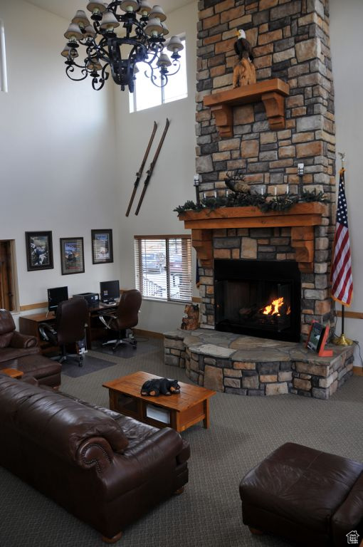 Carpeted living area with a towering ceiling, a chandelier, an office area, and a stone fireplace