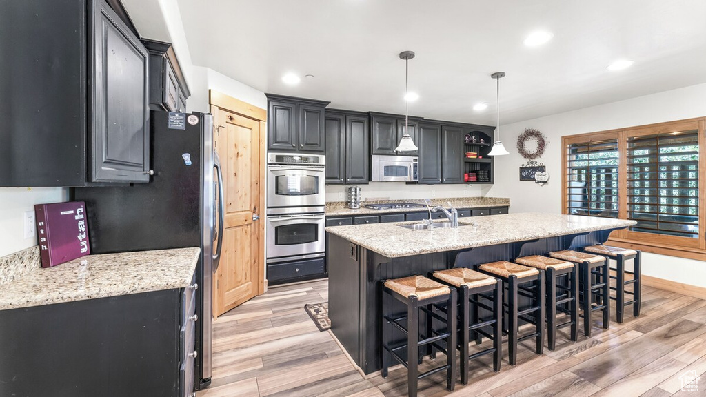 Kitchen with stainless steel appliances, light wood-type flooring, a kitchen breakfast bar, recessed lighting, and a center island with sink