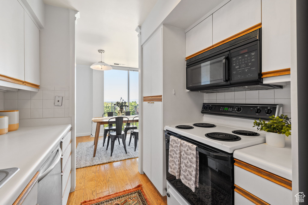 Kitchen featuring white electric range oven, black microwave, light wood-style flooring, backsplash, and white cabinetry