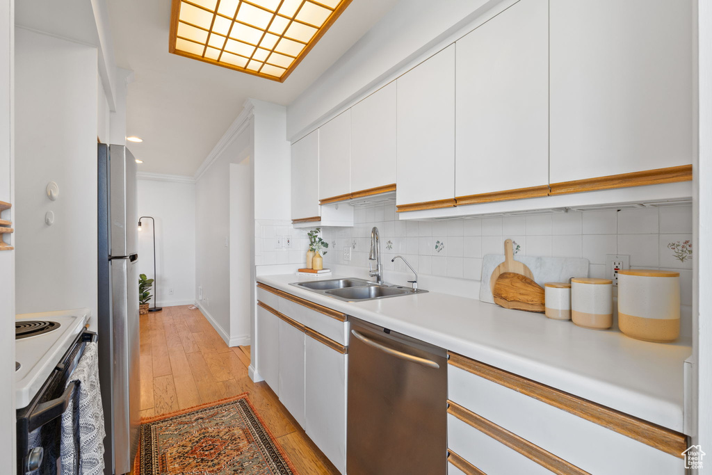 Kitchen featuring stainless steel appliances, tasteful backsplash, light countertops, white cabinetry, and light wood-type flooring