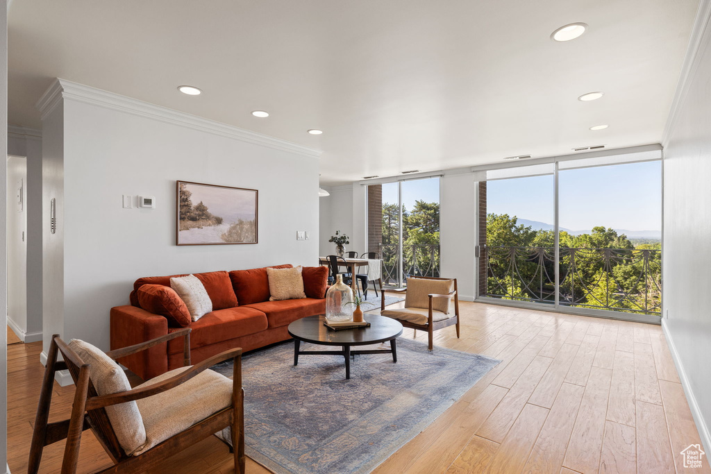 Living room with ornamental molding, light wood-type flooring, recessed lighting, and a wall of windows