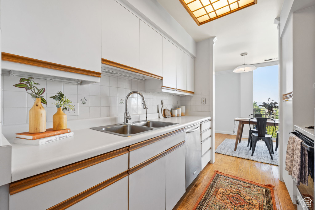 Kitchen with light wood-type flooring, stainless steel dishwasher, white electric stove, white cabinetry, and decorative backsplash