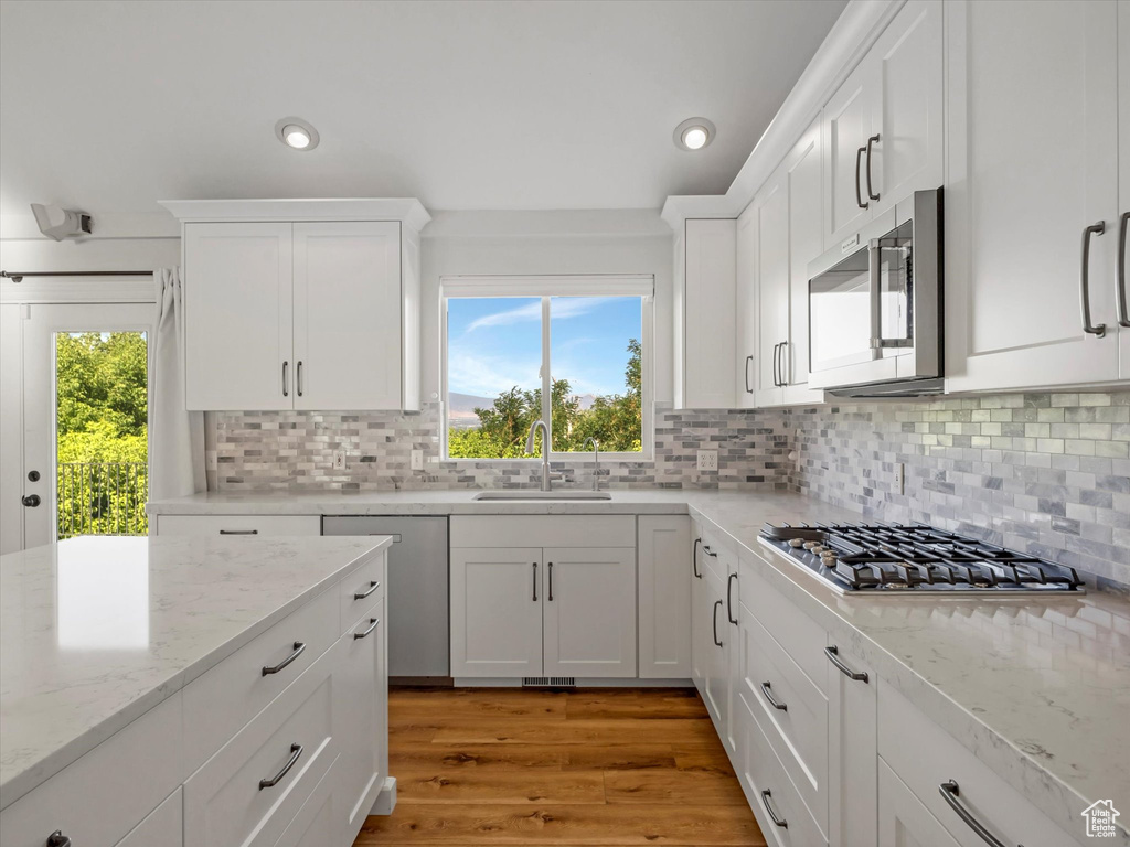 Kitchen with stainless steel appliances, white cabinetry, recessed lighting, tasteful backsplash, and light stone countertops