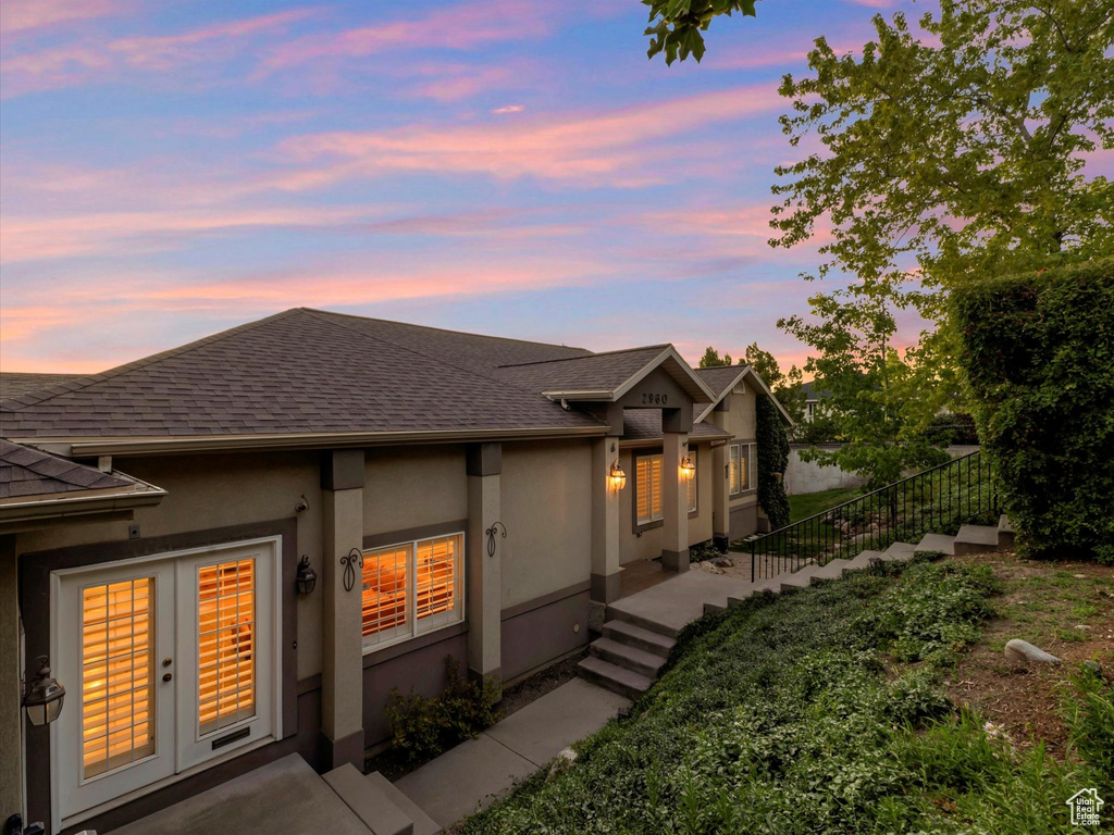 View of front of home with roof with shingles, stucco siding, and french doors