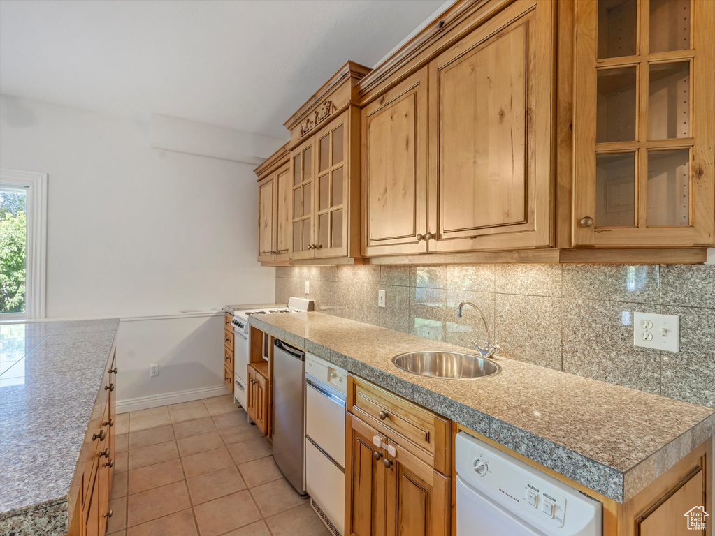 Kitchen with white dishwasher, backsplash, glass insert cabinets, and light tile patterned floors