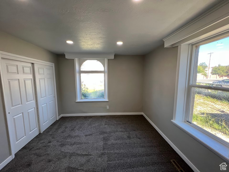 Unfurnished bedroom featuring dark carpet, multiple windows, a closet, recessed lighting, and a textured ceiling