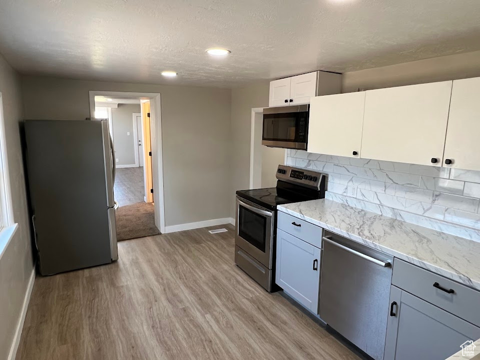 Kitchen with stainless steel appliances, light wood finished floors, decorative backsplash, light stone counters, and a textured ceiling