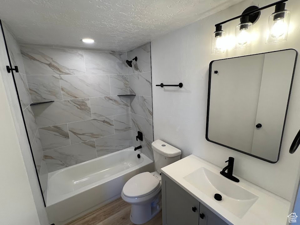 Full bathroom with a textured ceiling, vanity, shower / bathtub combination, and wood finished floors