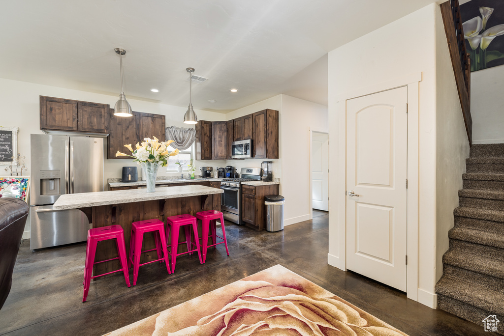 Kitchen with appliances with stainless steel finishes, a breakfast bar area, dark brown cabinets, recessed lighting, and hanging light fixtures