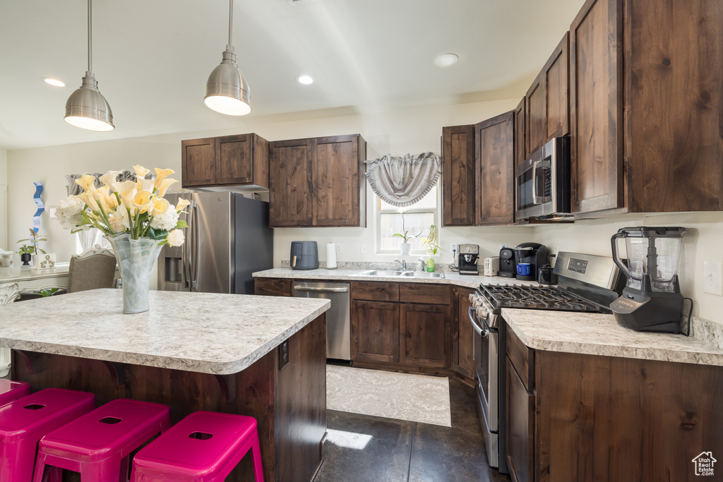 Kitchen featuring stainless steel appliances, light countertops, dark brown cabinets, a kitchen island, and recessed lighting