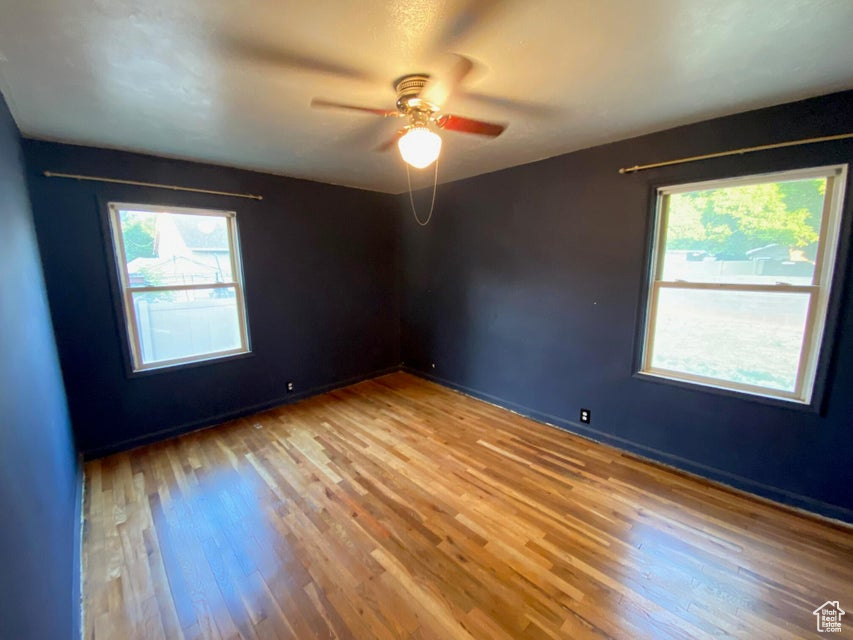 Empty room with plenty of natural light, wood finished floors, and a ceiling fan