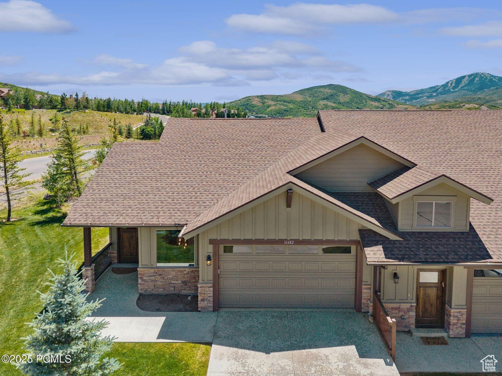 View of front of house with board and batten siding, a garage, stone siding, roof with shingles, and driveway
