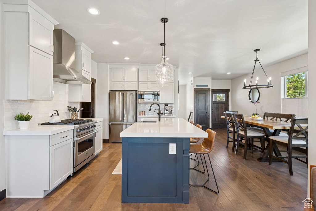 Kitchen with appliances with stainless steel finishes, wall chimney exhaust hood, light countertops, backsplash, and recessed lighting