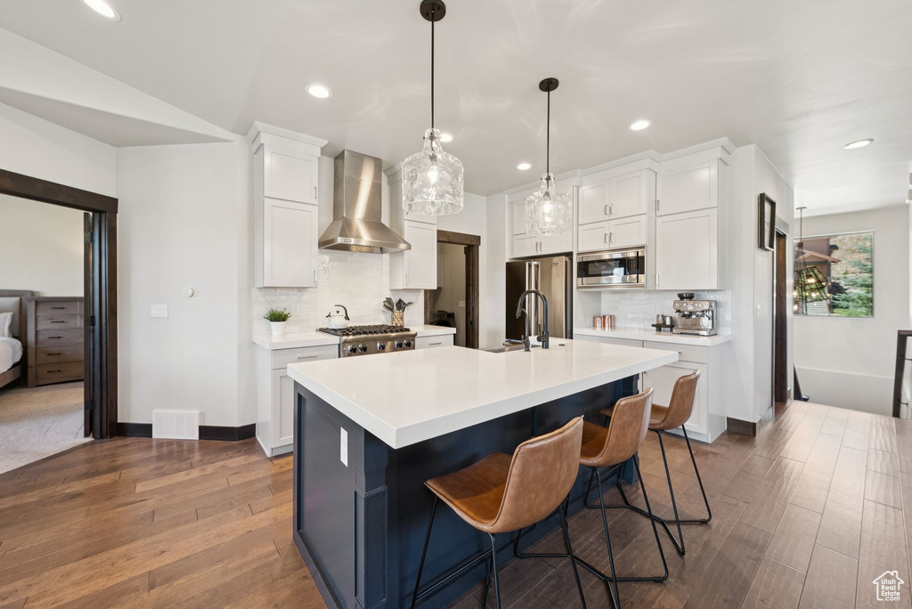 Kitchen featuring wall chimney exhaust hood, appliances with stainless steel finishes, tasteful backsplash, light countertops, and wood finished floors