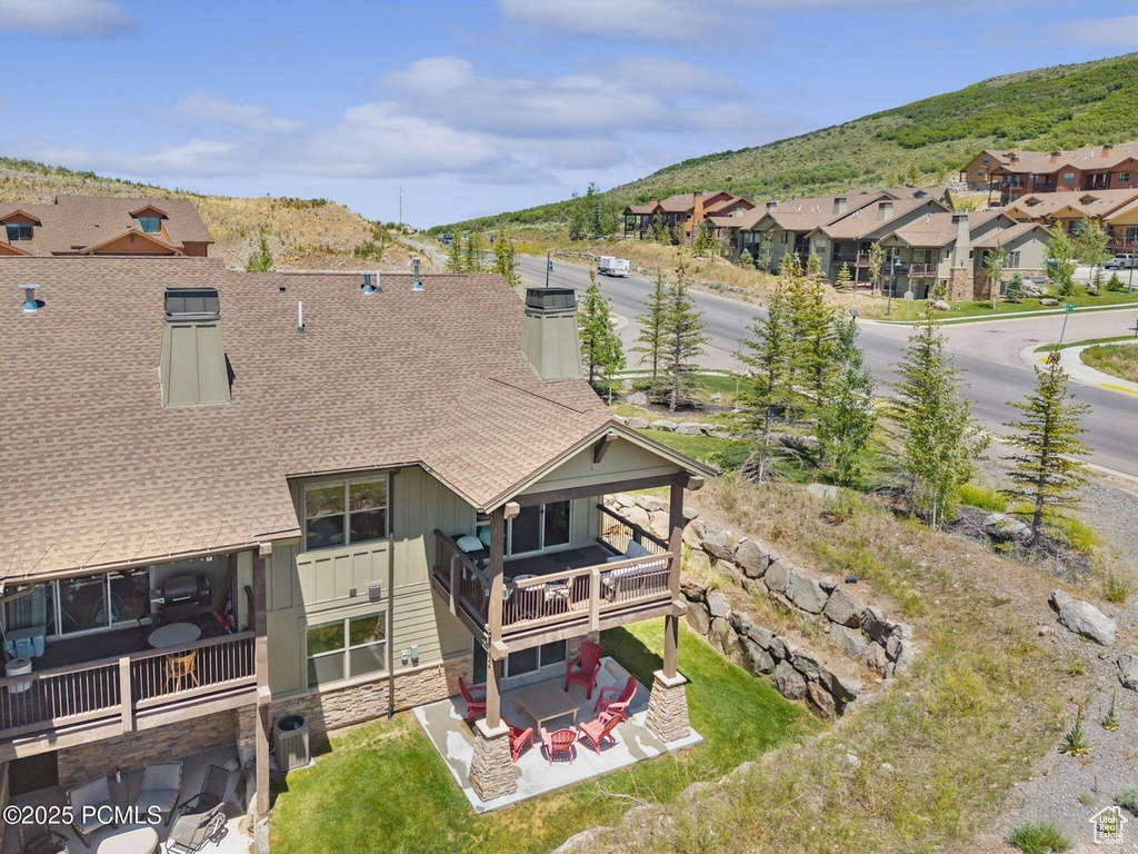 Back of property with roof with shingles, stone siding, a mountain view, a patio area, and a residential view
