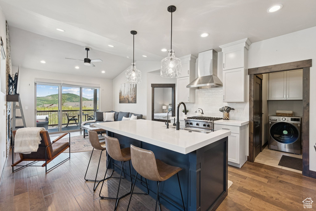 Kitchen featuring washer / clothes dryer, wall chimney range hood, open floor plan, white cabinets, and lofted ceiling