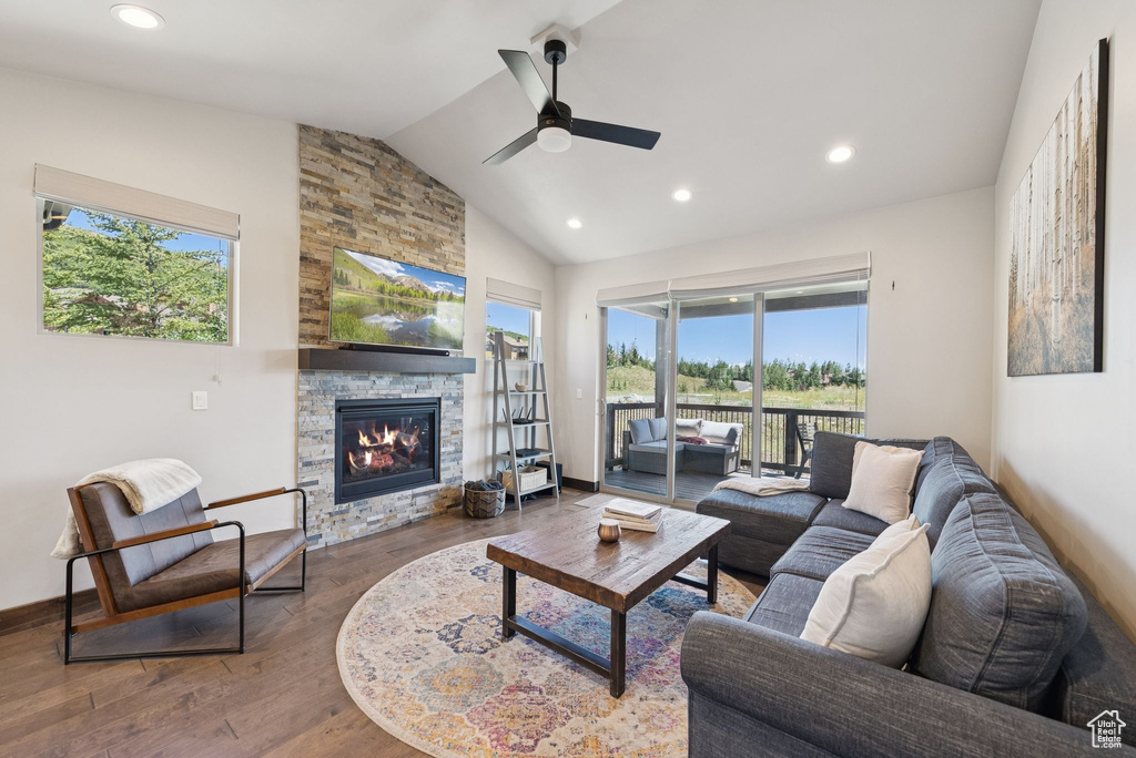Living room featuring wood finished floors, ceiling fan, lofted ceiling, a stone fireplace, and recessed lighting