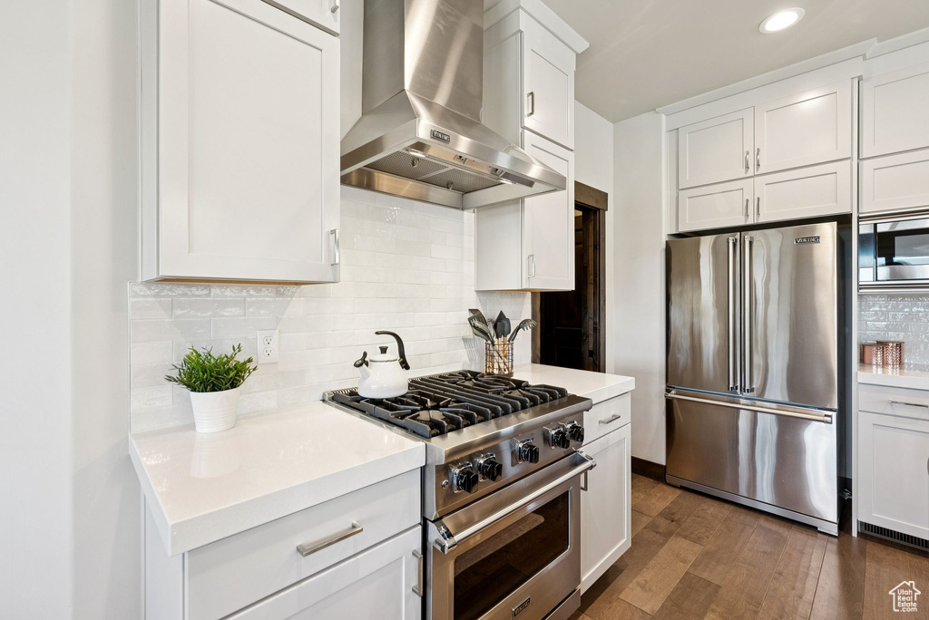 Kitchen featuring premium appliances, extractor fan, dark wood-style flooring, white cabinets, and light countertops