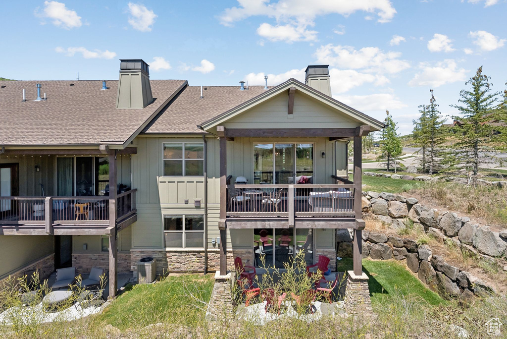 Back of house with a chimney, board and batten siding, stone siding, and a shingled roof