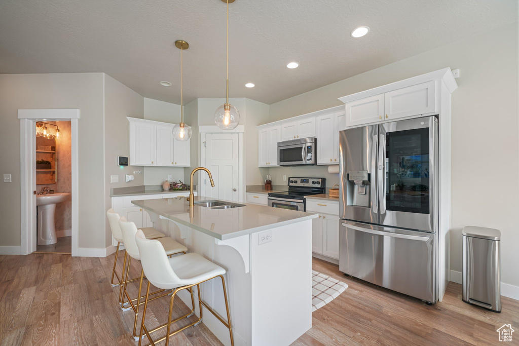 Kitchen with appliances with stainless steel finishes, light wood finished floors, an island with sink, white cabinetry, and recessed lighting