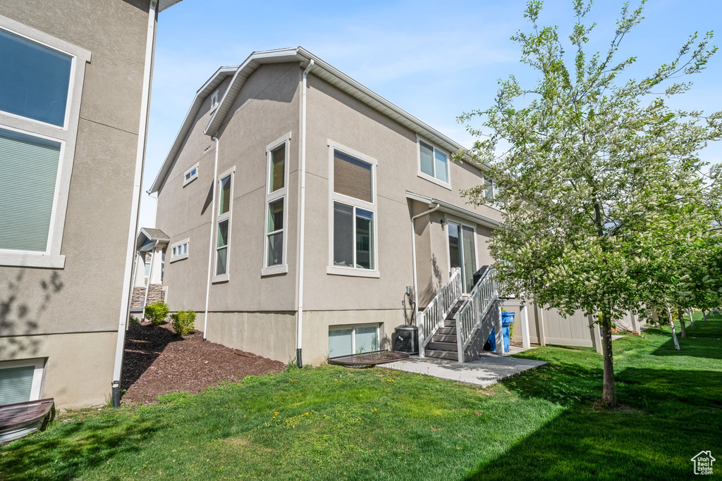 Rear view of house with stucco siding, a yard, and stairs