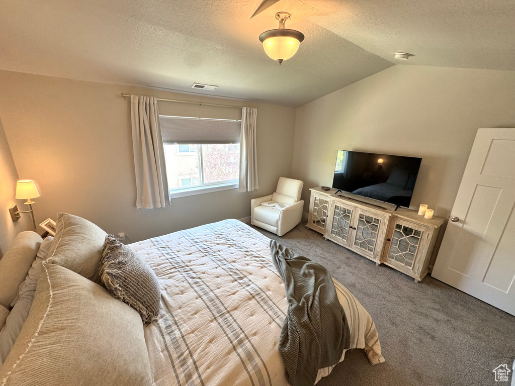 Carpeted bedroom featuring a textured ceiling and vaulted ceiling