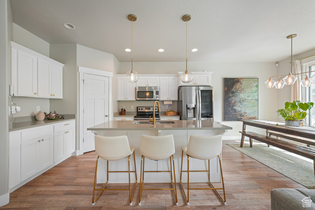 Kitchen featuring appliances with stainless steel finishes, a center island with sink, light wood-style flooring, white cabinetry, and recessed lighting
