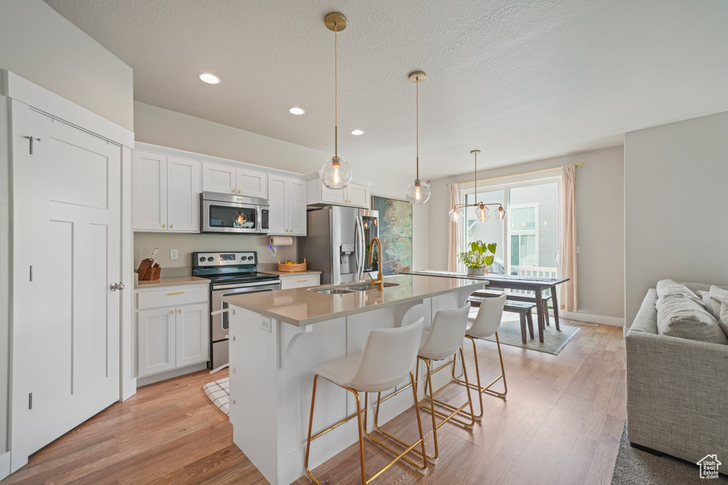 Kitchen with stainless steel appliances, recessed lighting, an island with sink, white cabinetry, and a kitchen bar