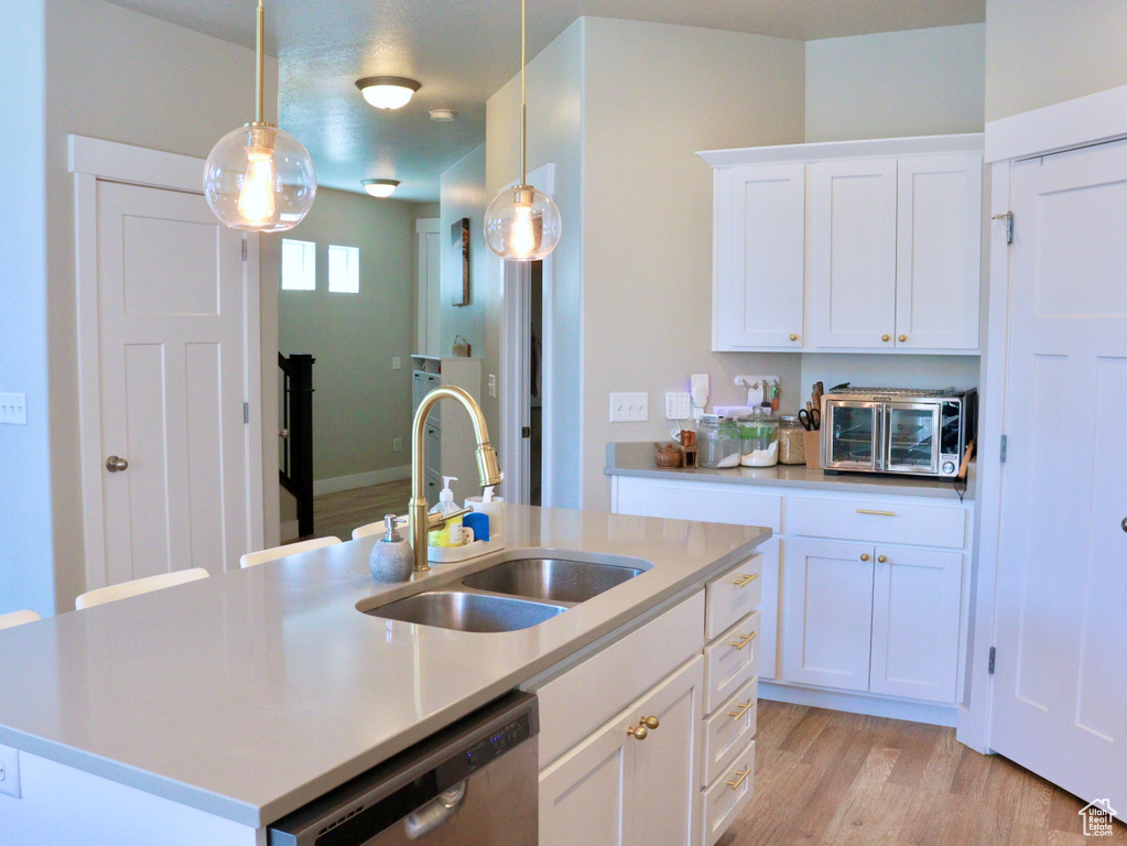 Kitchen with stainless steel dishwasher, light wood-style floors, pendant lighting, white cabinets, and a kitchen island with sink