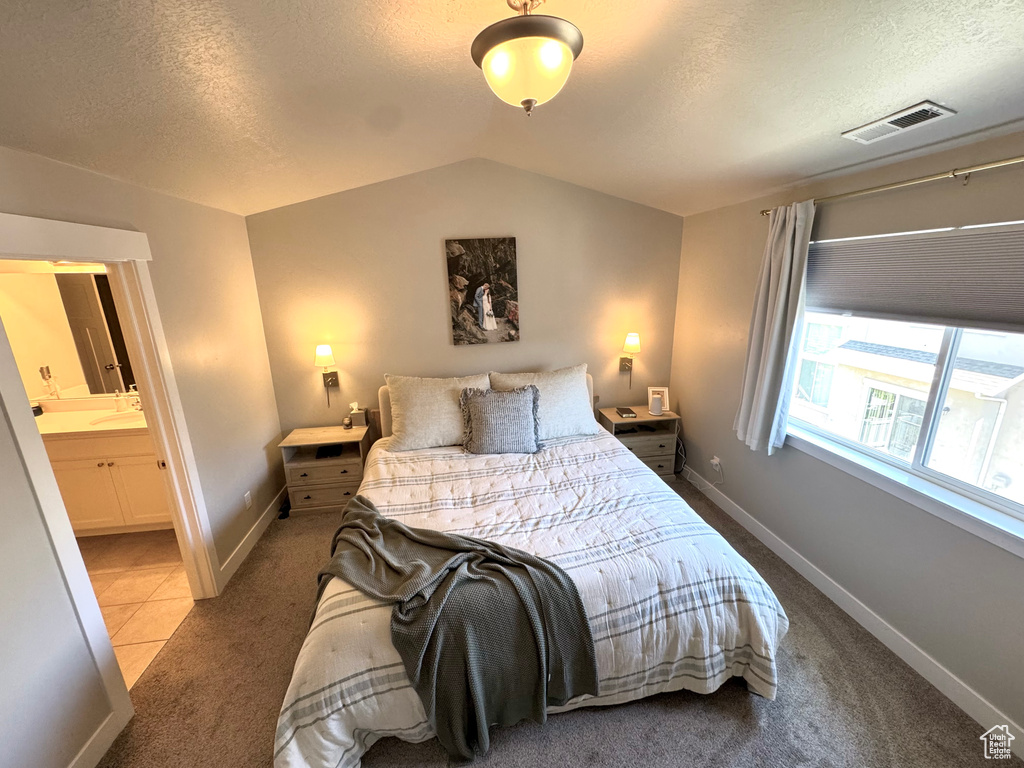 Carpeted bedroom featuring a textured ceiling, vaulted ceiling, and ensuite bathroom