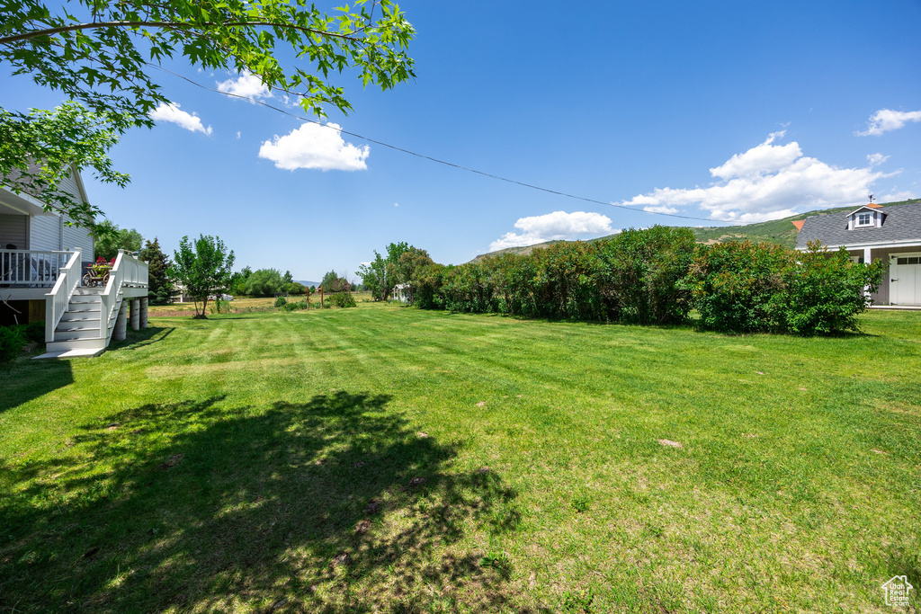 View of grassy yard with a wooden deck and stairs