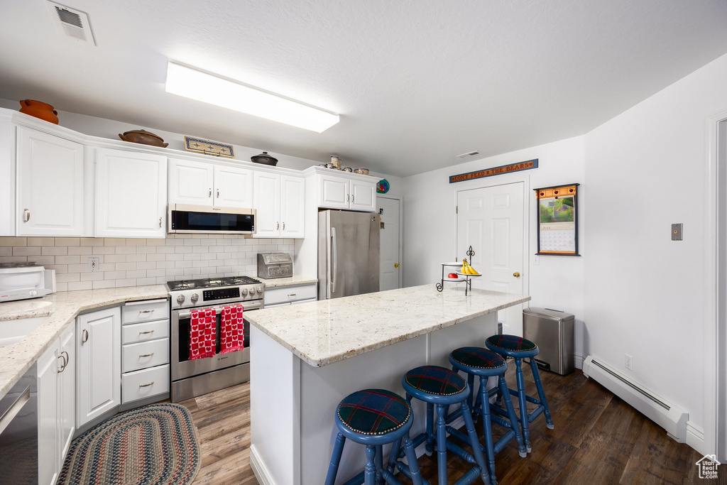 Kitchen featuring stainless steel appliances, a baseboard heating unit, dark wood-type flooring, and white cabinets