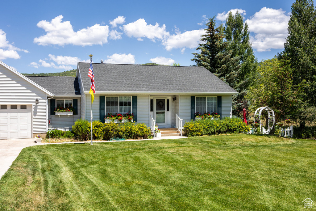 Ranch-style home featuring a front lawn, concrete driveway, a shingled roof, and a garage