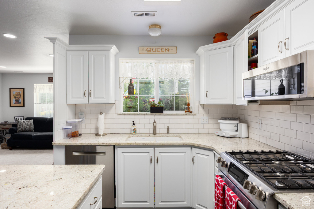 Kitchen with stainless steel appliances, white cabinets, decorative backsplash, light stone counters, and recessed lighting