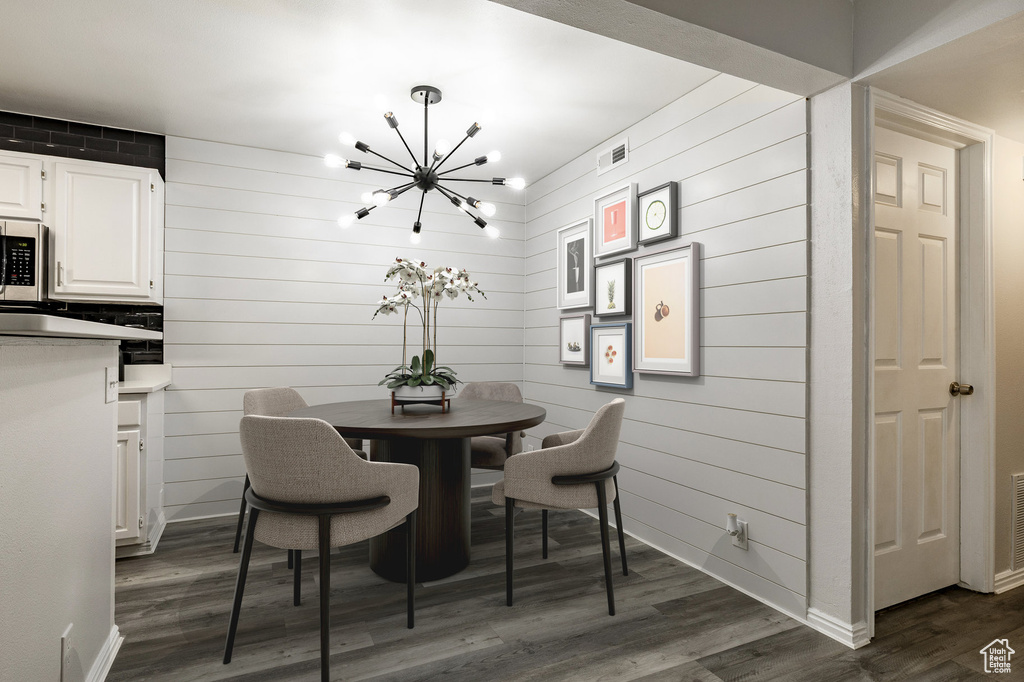 Dining space with a chandelier, dark wood-type flooring, and wooden walls