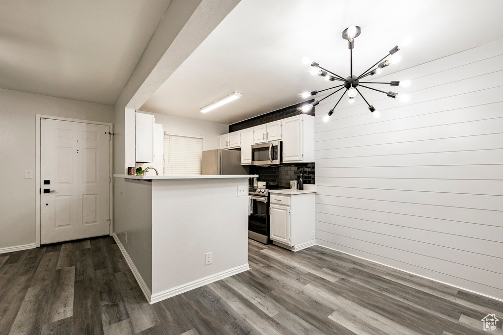 Kitchen featuring stainless steel appliances, a chandelier, dark wood-type flooring, tasteful backsplash, and white cabinets