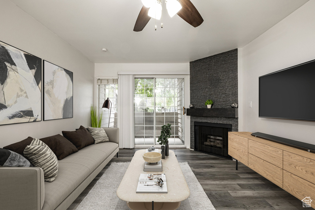 Living area featuring a ceiling fan, dark wood-style floors, and a stone fireplace