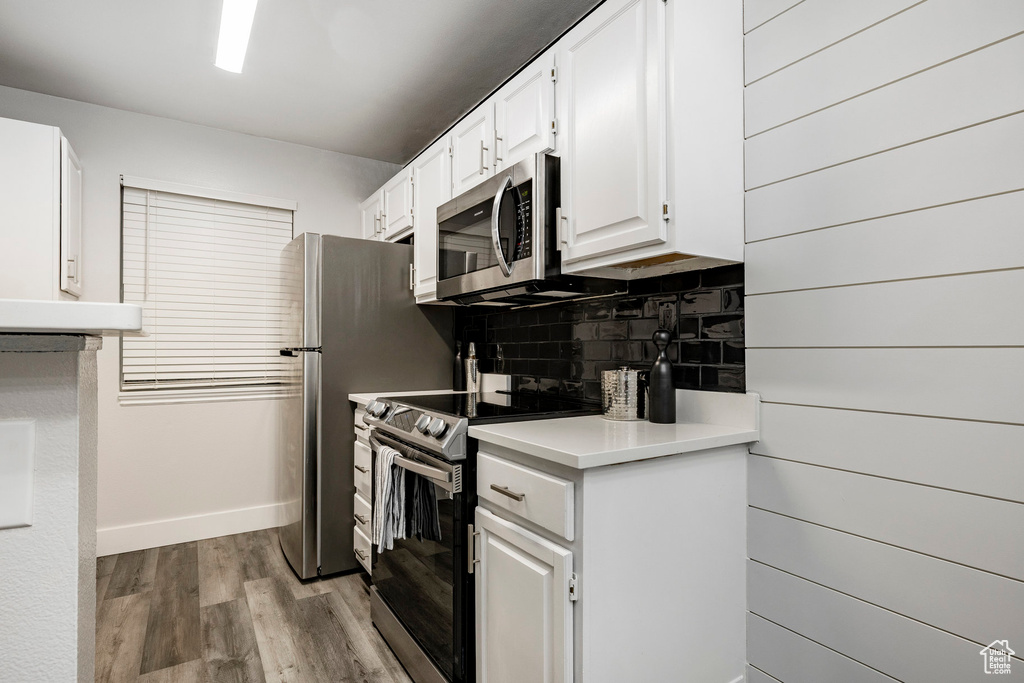 Kitchen with appliances with stainless steel finishes, backsplash, wood finished floors, light countertops, and white cabinetry