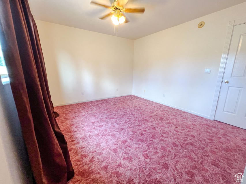 Carpeted empty room with ceiling fan and baseboards
