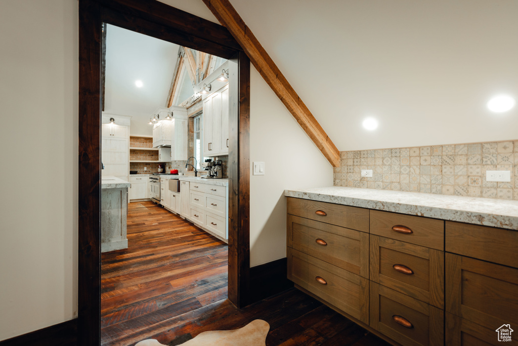 Kitchen with vaulted ceiling, tasteful backsplash, dark wood-type flooring, light stone counters, and white cabinetry