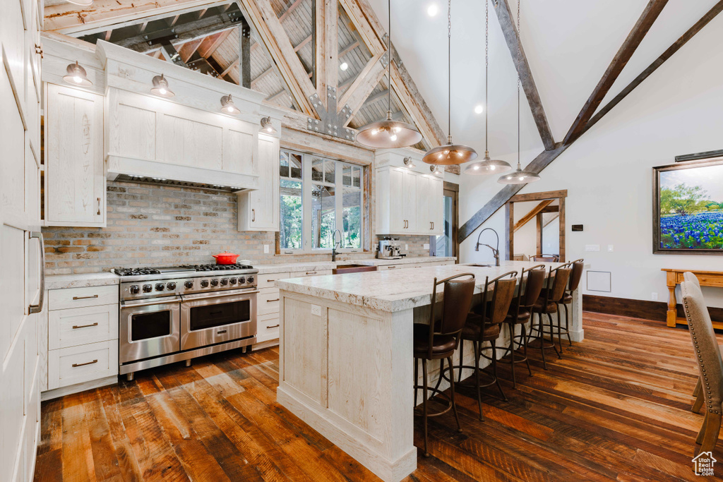 Kitchen featuring range with two ovens, dark wood-style flooring, high vaulted ceiling, decorative backsplash, and a kitchen breakfast bar