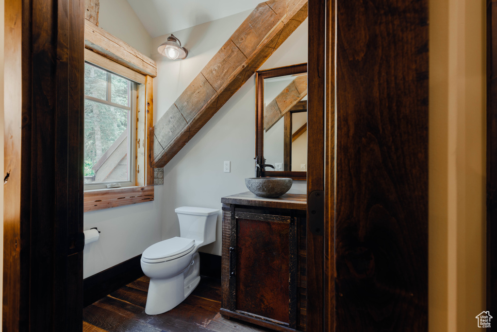 Half bathroom featuring vaulted ceiling, vanity, and wood finished floors