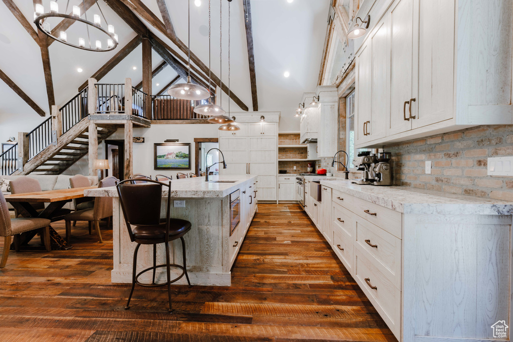 Kitchen featuring high vaulted ceiling, beamed ceiling, a chandelier, decorative backsplash, and an island with sink